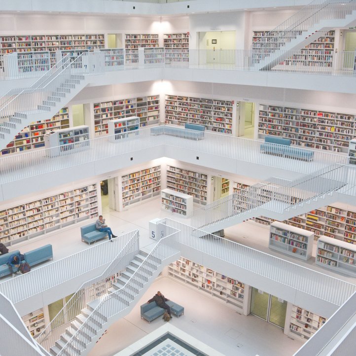 helle, mehrstöckige Bibliothek mit einem Atrium in der Mitte und vielen Bücherregalen an den Seiten, auf blauen Sofas in jeder Etage sitzen Menschen 