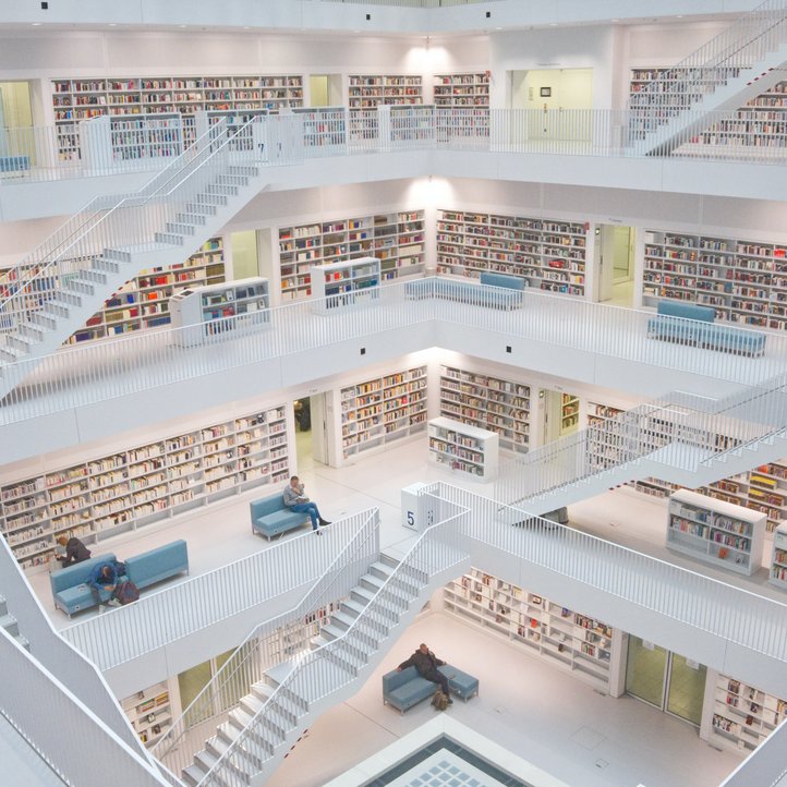helle, mehrstöckige Bibliothek mit einem Atrium in der Mitte und vielen Bücherregalen an den Seiten, auf blauen Sofas in jeder Etage sitzen Menschen 